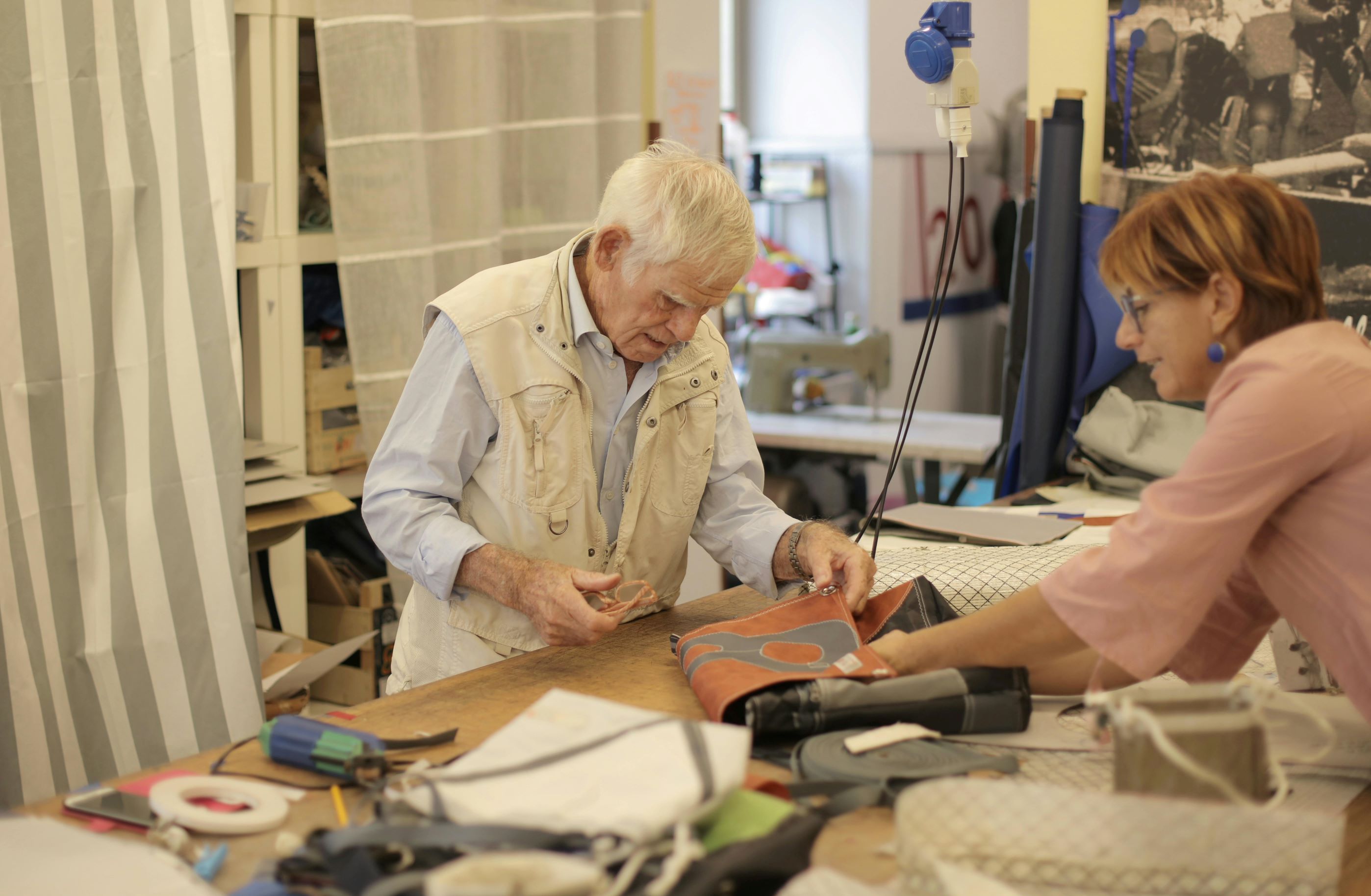Senior craftsman making leather bad in workshop with assistant.